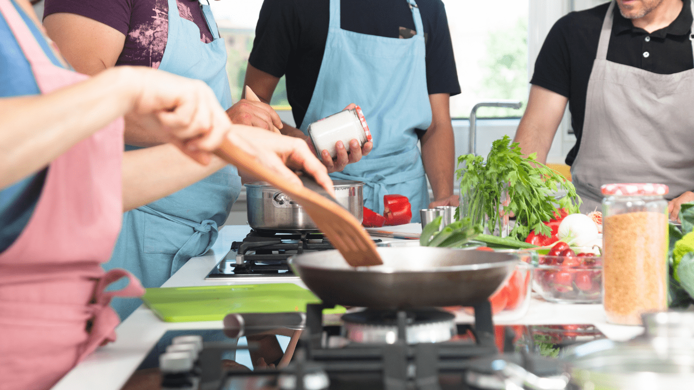 A group of people cooking together in a kitchen during an NDIS dietetic consultation, preparing healthy meals.