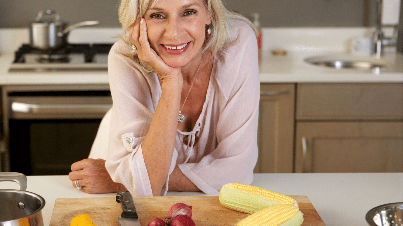 A middle-aged woman and a dietitian sitting together at a kitchen counter, discussing a balanced meal plan surrounded by fresh fruits, vegetables, and whole grains.