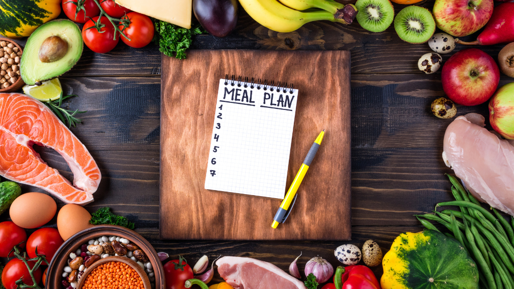 A balanced meal with grilled salmon, quinoa, spinach, sweet potato, and broccoli, surrounded by herbal teas, turmeric, and a notepad with a meal plan, representing nutrition for managing endometriosis.